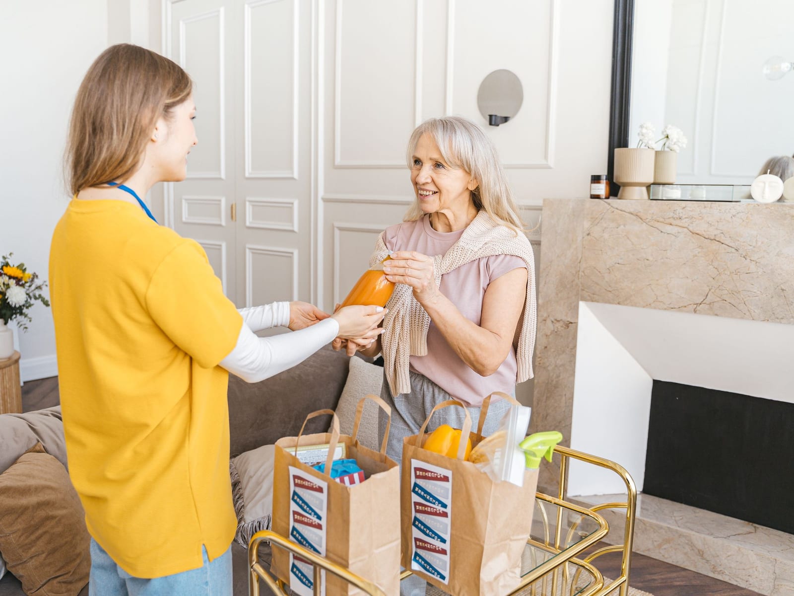 A support professional hands a woman a bottle of juice as they put away groceries in her living room.